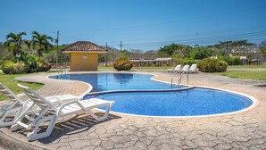 Piscina com espreguiçadeiras, um pequeno edifício e vegetação ao redor.