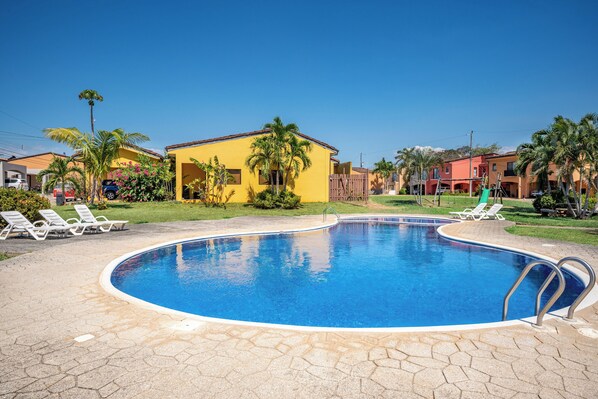 A swimming pool with a curved edge, surrounded by lounge chairs and palm trees, with buildings in the background. - 3 Mi to Tamarindo & Beach: Cozy 2BR Home (Tamarindo)