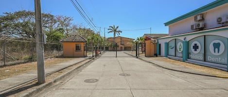 Une vue de rue avec une clinique dentaire sur la droite, une entrée fermée par un portail et un ciel dégagé.