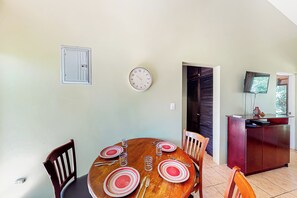 Een eethoek met een ronde tafel, stoelen, borden, bestek en een wandklok.