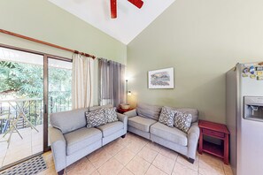 A living room with a grey sofa, a small table, a refrigerator, and a window with curtains. - Playa Ocotal Condo w/ Pool: Walk to the Beach! (Playa Ocotal)