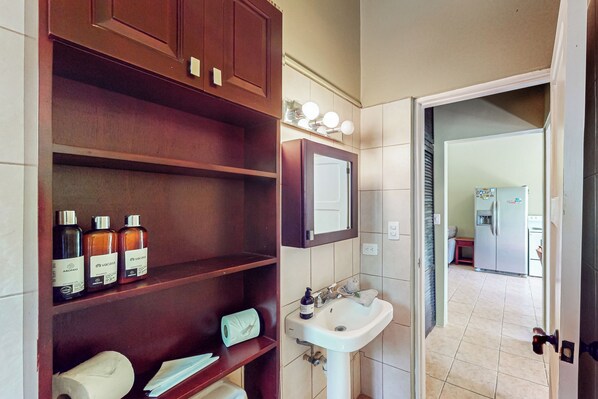 A bathroom with a wooden vanity, a sink, and a mirror. There are toiletries on the vanity and a towel on the floor. - Playa Ocotal Condo w/ Pool: Walk to the Beach! (Playa Ocotal)