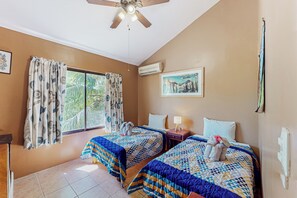 Een hotelkamer met twee bedden, een plafondventilator, een airconditioning en een raam met gordijnen.
