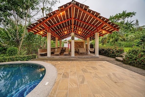A covered outdoor seating area with a pool. - Lush Jungle Home w/ Chemical-Free Pool & Bar! (Grecia)