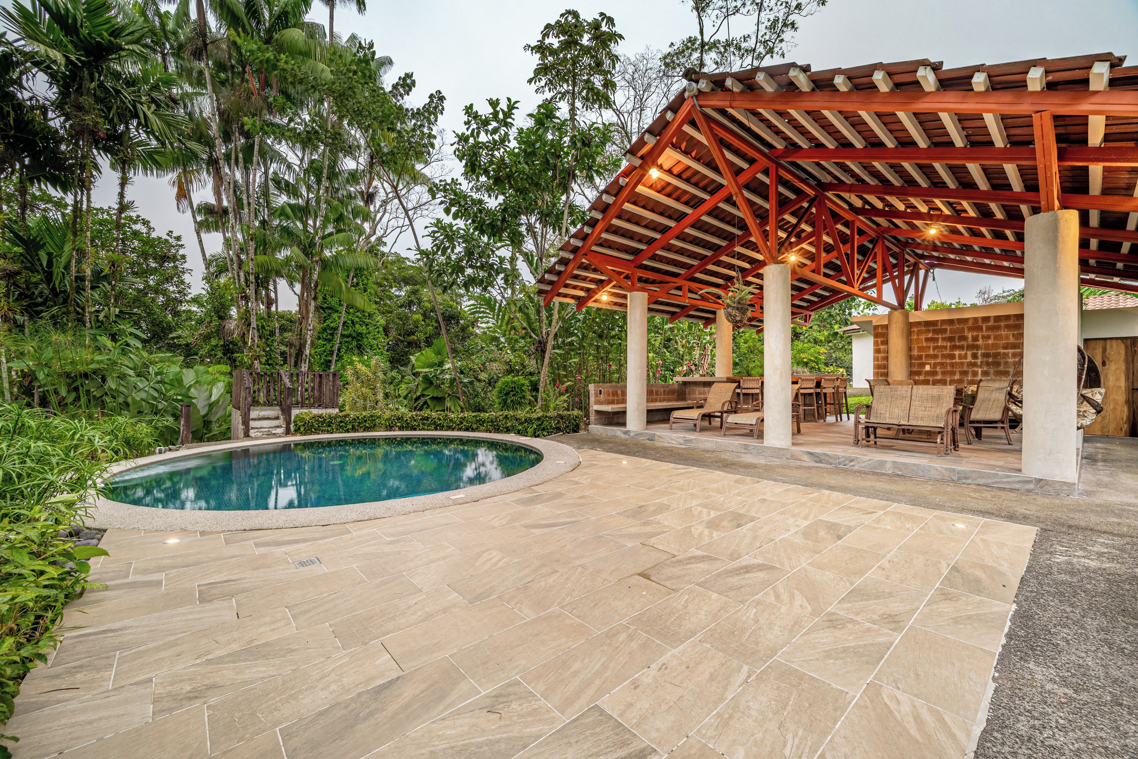 A pool area with a pergola, lounge chairs, and a stone patio.