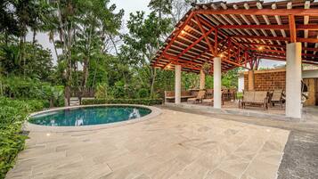 A pool area with a pergola, lounge chairs, and a stone patio.
