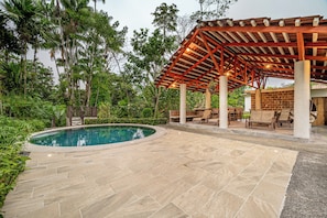 A pool area with a pergola, lounge chairs, and a stone patio.