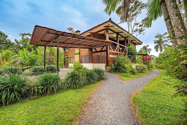 A wooden house with a gravel pathway leading to it, surrounded by lush greenery. - Lush Jungle Home w/ Chemical-Free Pool & Bar! (Grecia)