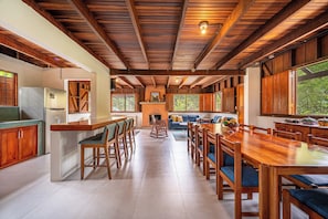 A spacious kitchen with wooden cabinets, a central island, and a dining area with a large wooden table and chairs. - Lush Jungle Home w/ Chemical-Free Pool & Bar! (Grecia)