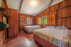 A wooden room with two beds, a large window, and a door leading outside. - Lush Jungle Home w/ Chemical-Free Pool & Bar! (Grecia)