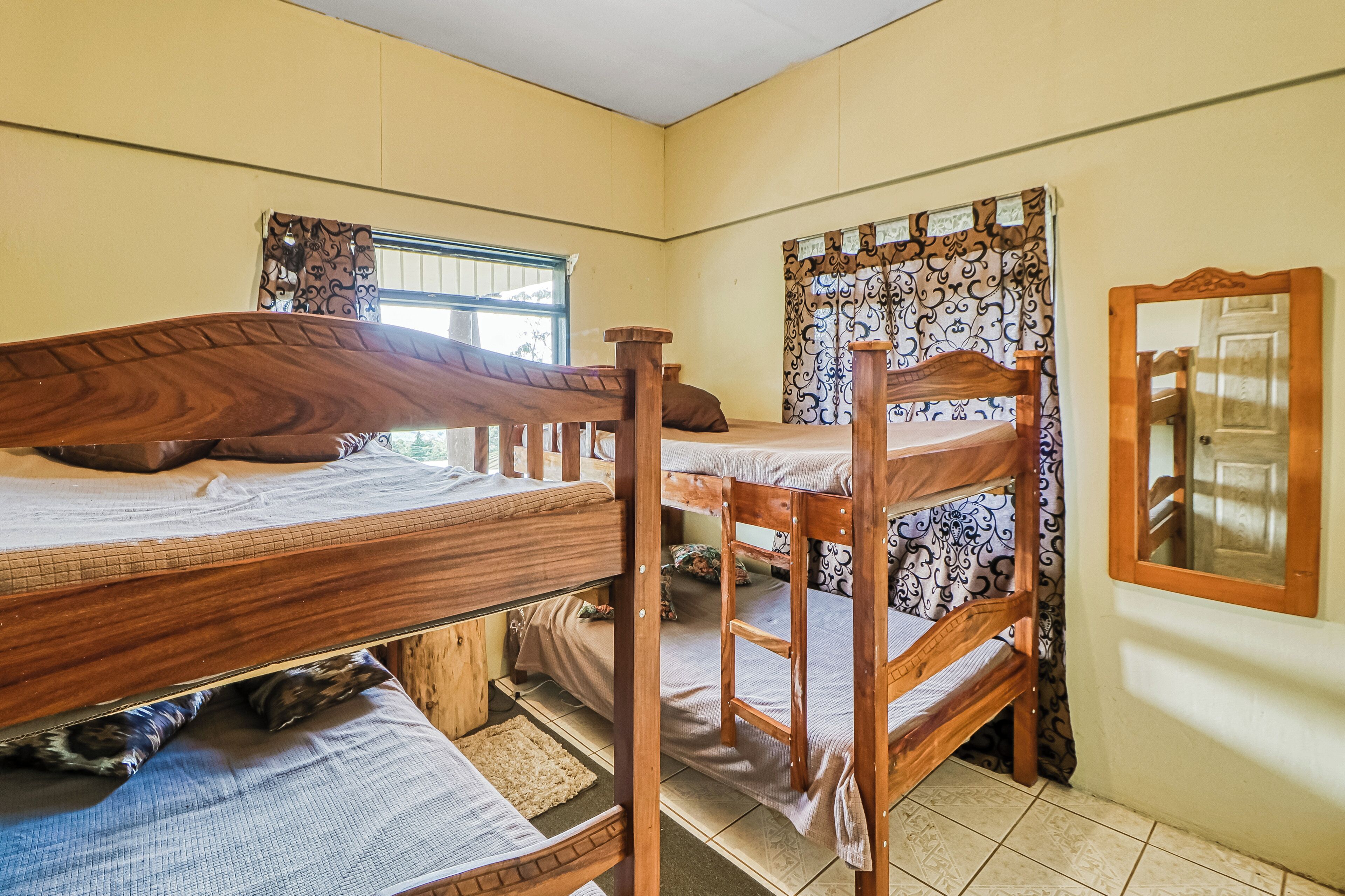 A bunk bed room with a window, curtains, and a mirror on the wall.
