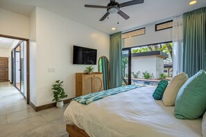 A bedroom with a bed, a ceiling fan, a TV, a window with curtains, and a view of a swimming pool. - Modern 4BR Family Home w/ Pool in Tamarindo (Tamarindo)