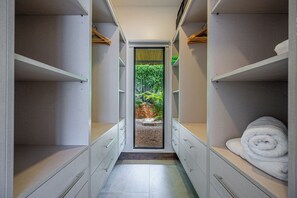 A walk-in closet with open shelves, a central door leading to a garden view, and a neatly folded towel on the right. - Modern 4BR Family Home w/ Pool in Tamarindo (Tamarindo)