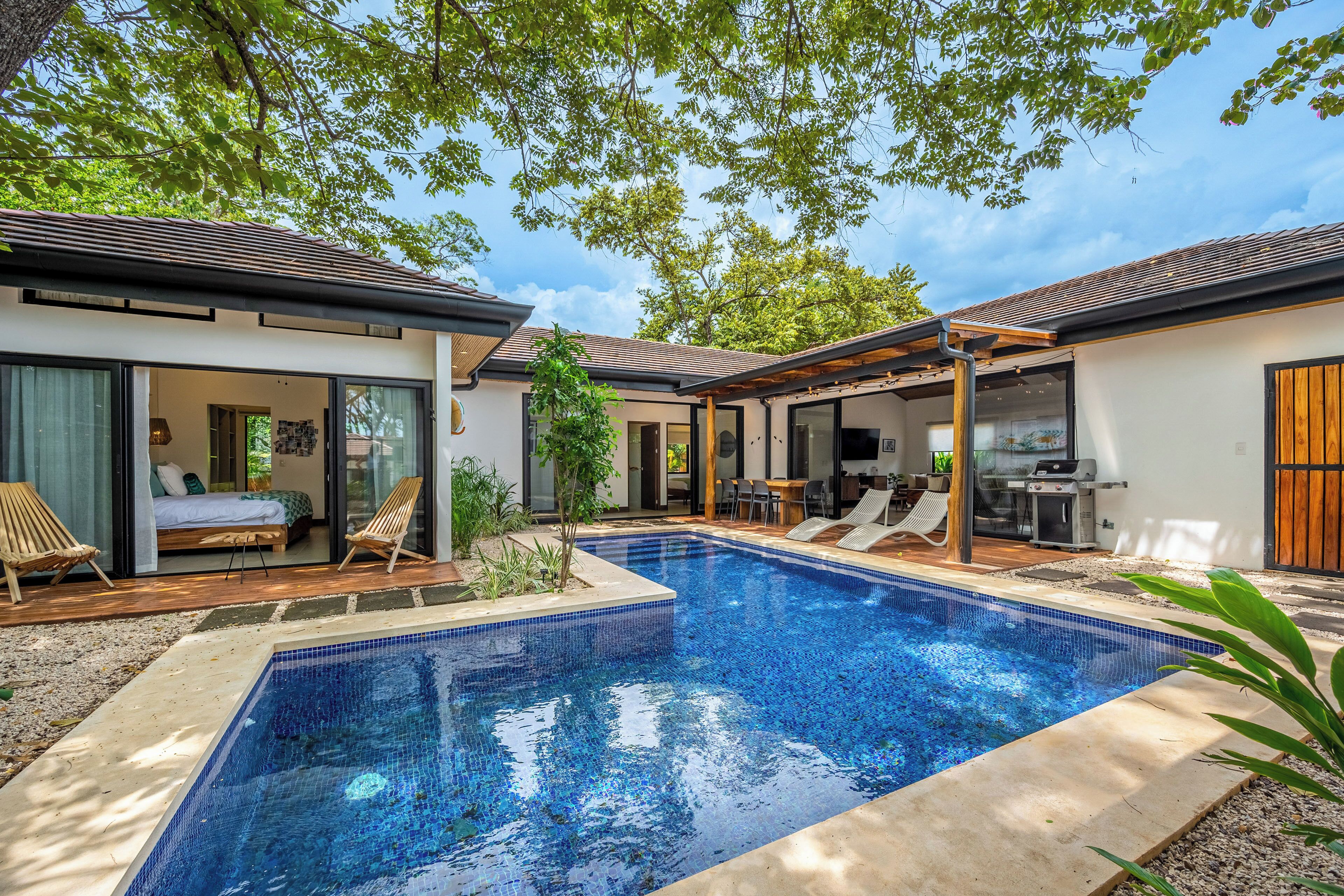 Un espace piscine extérieur moderne, doté d’une piscine à l’eau d’un bleu limpide, d’une terrasse en bois et de chaises longues.