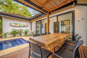 A modern outdoor dining area with a wooden table and chairs, a glass-enclosed space, and a decorative wall piece. - Modern 4BR Family Home w/ Pool in Tamarindo (Tamarindo)