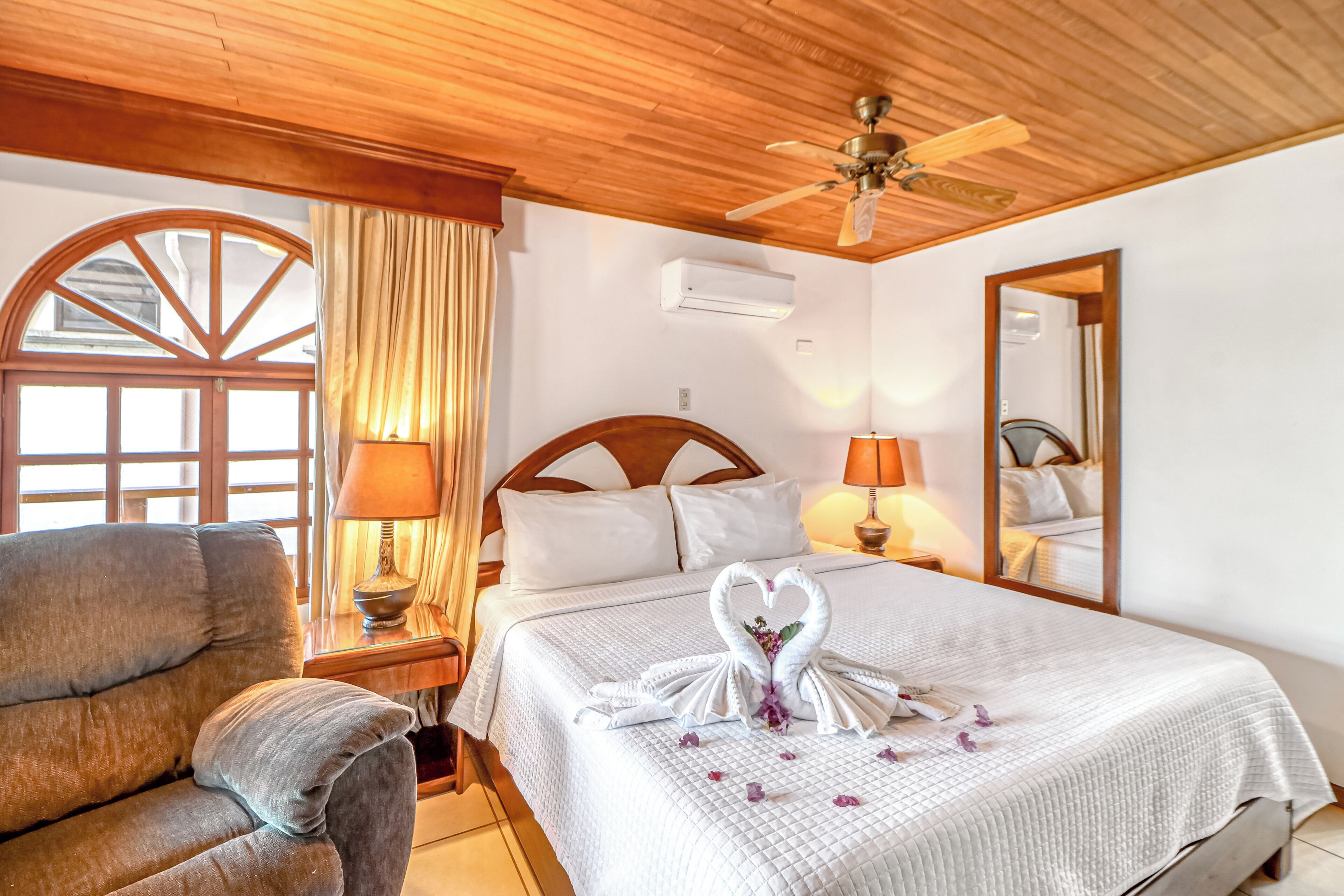 Habitación de hotel con cama, una silla, ventilador de techo, aire acondicionado y un espejo grande.