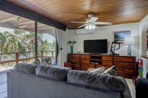 Een woonkamer met een bank, televisie, houten kast en een plafondventilator.