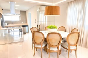 A modern kitchen with a dining area, featuring a round table with chairs, a hanging light fixture, and a potted plant. - ASA Cobertura Duplex Meia Praia Hidro 4QT (Itapema)