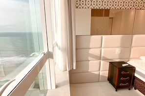 A hotel room with a large window overlooking the sea, a bed with a headboard, a small cabinet, and a patterned wall. - ASA Cobertura Duplex Meia Praia Hidro 4QT (Itapema)
