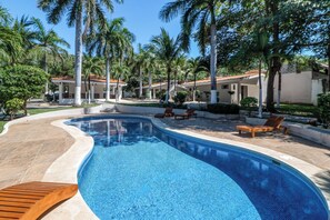 A swimming pool with a curved edge, surrounded by palm trees and lounge chairs. - Studio w/ Resort-Style Pool, Walk to Beach! (Playas del Coco)