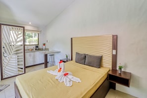 Ein Hotelzimmer mit Bett, Nachttisch, kleinem Tisch, Fenster und einer Küchenzeile.