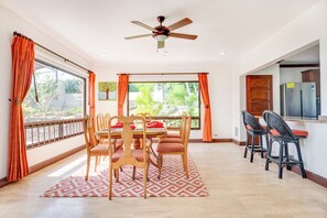 A dining area with a ceiling fan, a dining table with chairs, and a view of the outdoors through large windows. - Private Pool, Mtn-View Veranda! 3BR Carrillo Home (Playas del Coco)