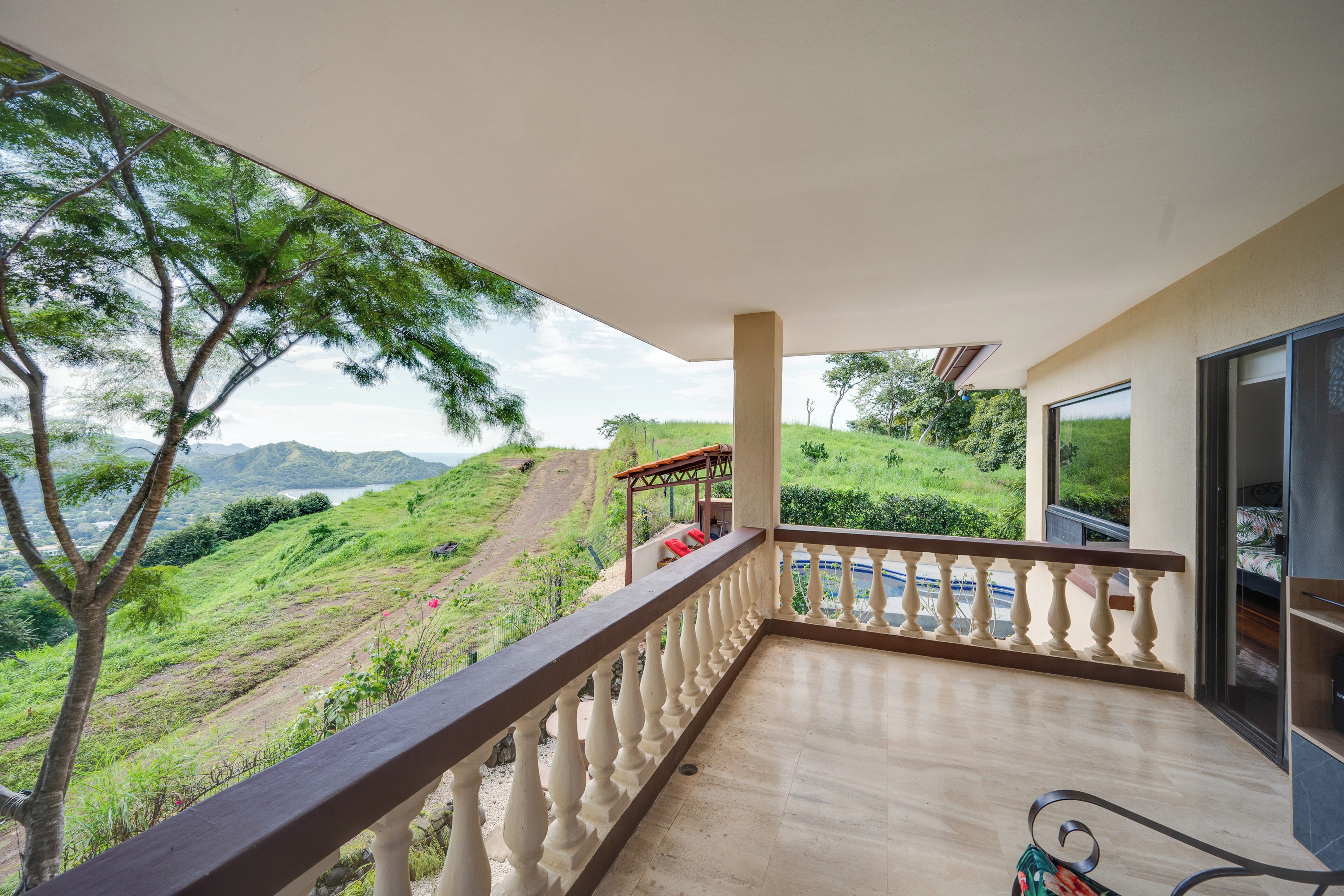 A balcony with a view of a hilly landscape and a body of water in the distance.
