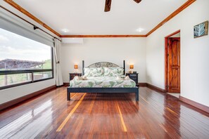 A bedroom with a large bed, wooden flooring, a window with a view, and a door. - Private Pool, Mtn-View Veranda! 3BR Carrillo Home (Playas del Coco)