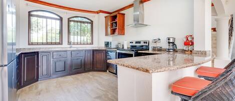 A spacious kitchen with dark cabinetry, a large island with bar stools, and a view through the windows.