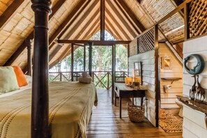 Une pièce avec un plafond en bois, un lit avec des oreillers, une table avec un panier, et une vue sur les arbres à l’extérieur.