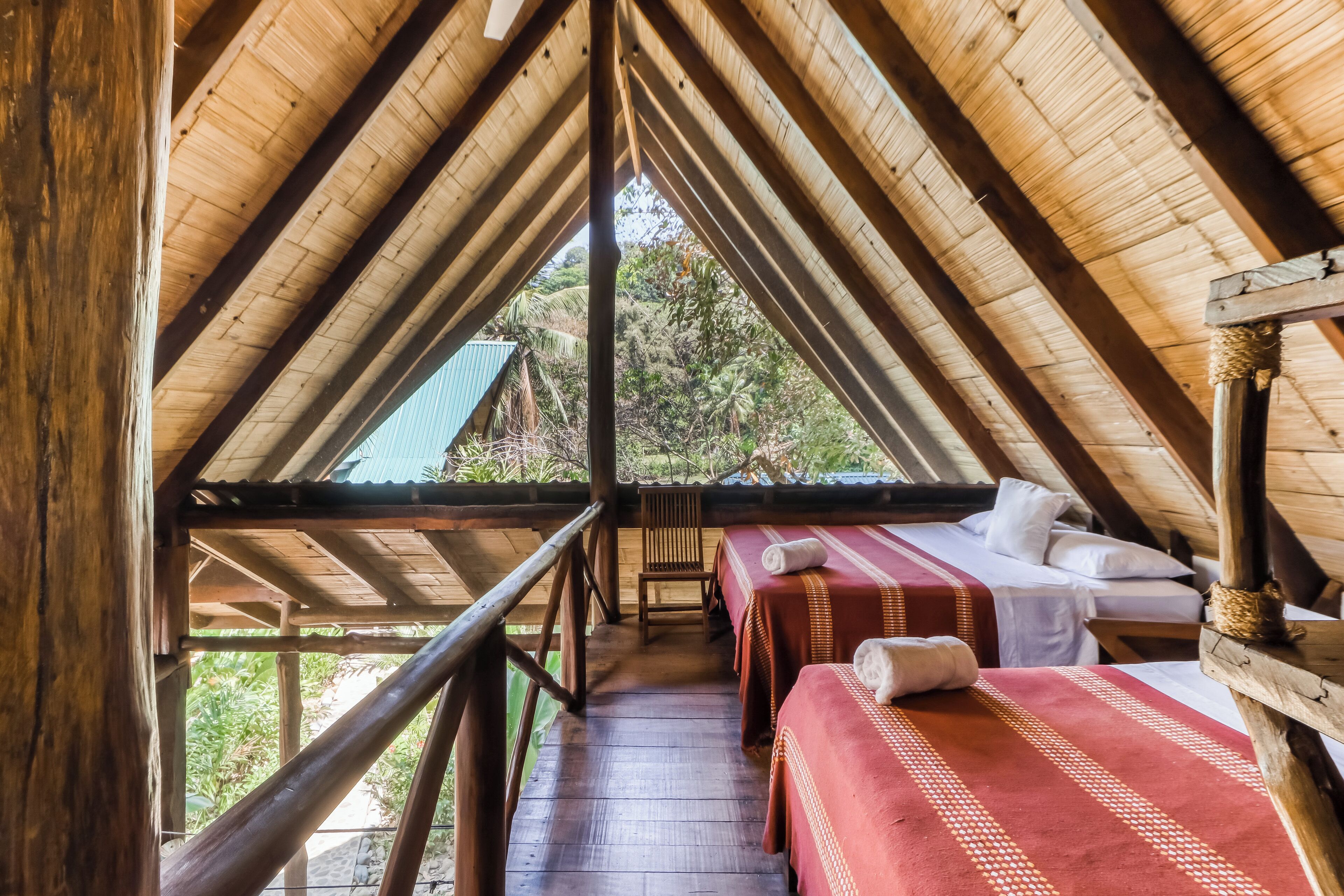 Een houten constructie met een schuin dak, een bed met een rode sprei en een bank.