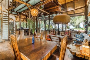Un coin repas en bois, avec une grande table et des chaises, intégré dans un intérieur rustique agrémenté de poutres apparentes et d’un luminaire suspendu.
