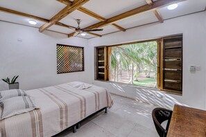 A bedroom with a bed, a chair, a ceiling fan, a window with a view of trees, and a small plant on the wall. - Award-Winning Oceanfront Home w/ Pool & Hot Tub! (La Javilla)
