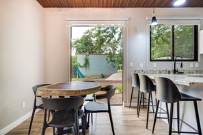 A modern kitchen with a wooden table and bar stools, a large window with a view of greenery, and a ceiling with wooden beams. - 5 Mi to Beach: Updated Playa Avellanas Gem (Playa Avellanas)