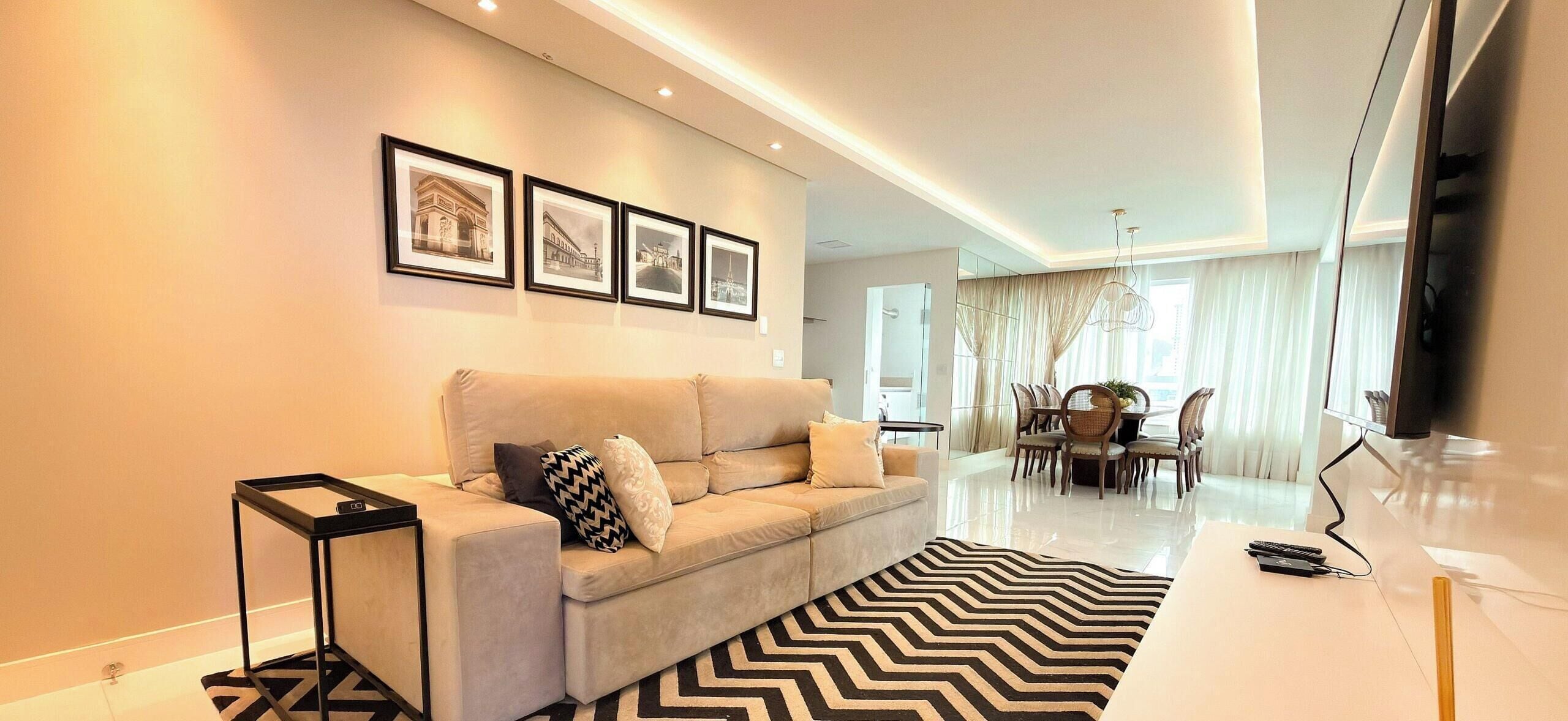 A modern living room with a sofa, a dining area with chairs, and framed pictures on the wall.