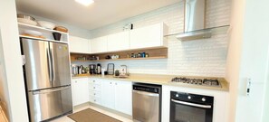 A modern kitchen with stainless steel appliances, white cabinetry, and a patterned backsplash. - ASA Cobertura Luxo 2QT Meia Praia Hidro (Itapema)