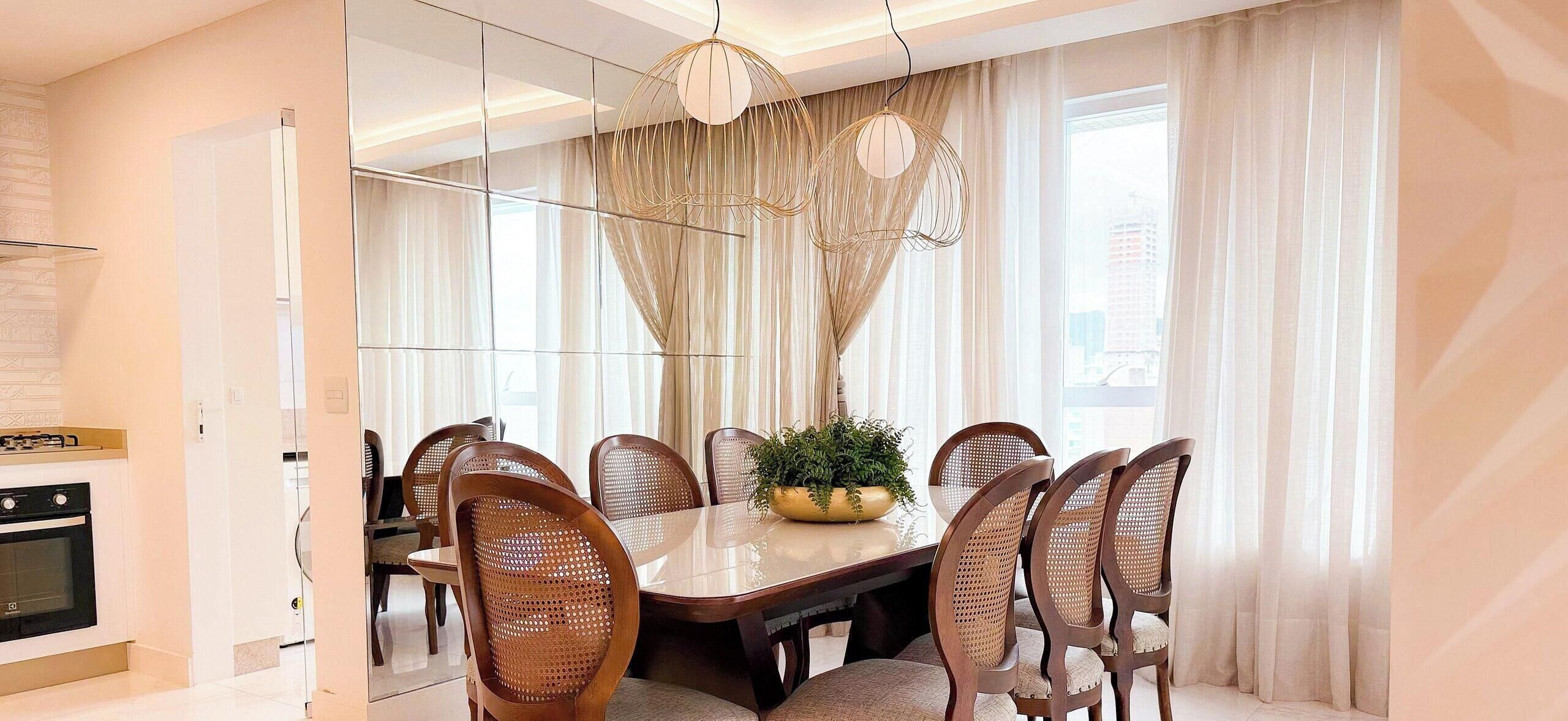 A dining area with a large table, six chairs, a potted plant, and a modern chandelier.