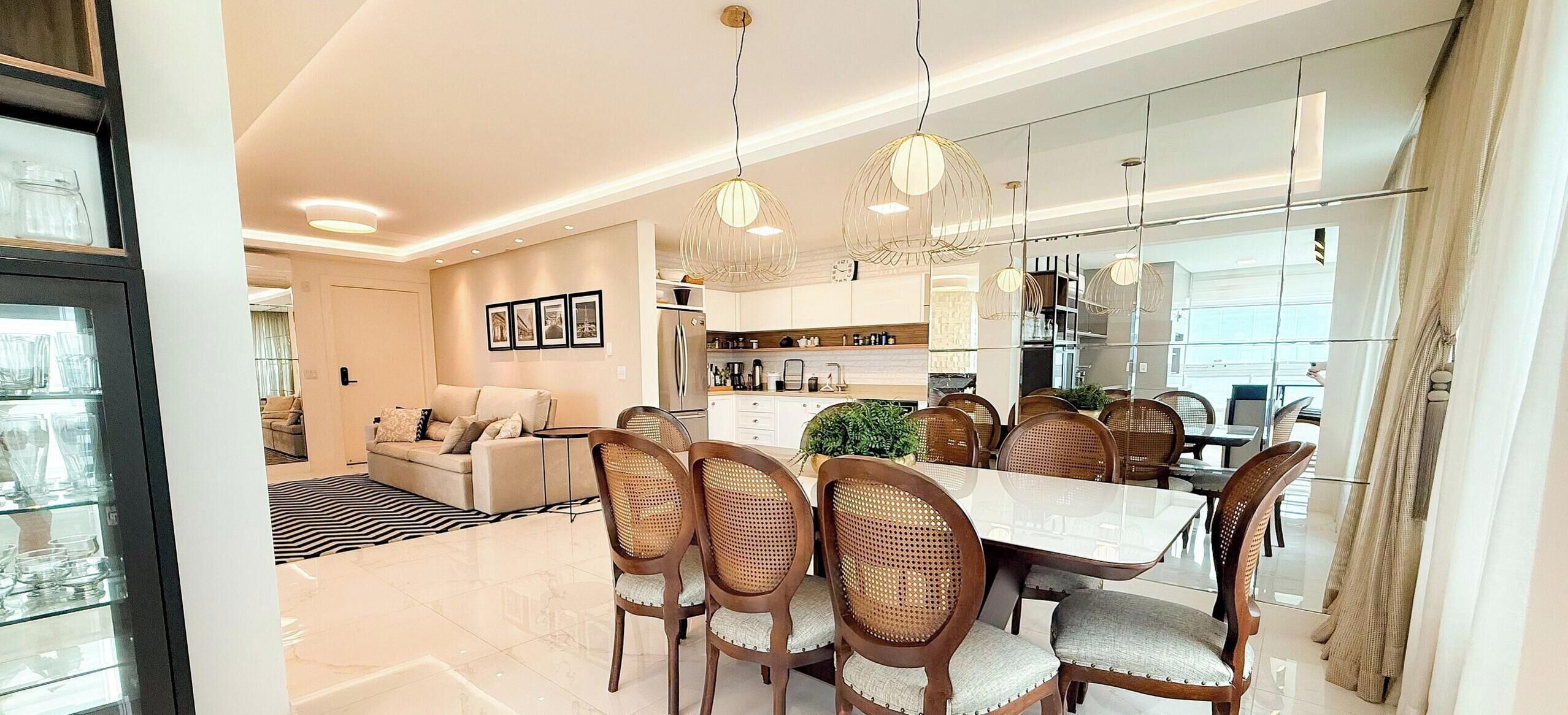 A modern dining area with a large table, wicker chairs, and pendant lighting.