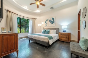 Ein Schlafzimmer mit Bett, Nachttisch, Kommode, Deckenventilator und Kunstwerken an der Wand.