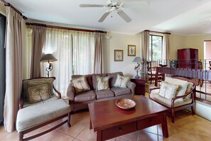 A living room with a sofa, two armchairs, a coffee table, a ceiling fan, and a view of the outdoors through a window. - Playa Conchal Resort Condo w/ Ocean View (Playa Conchal)