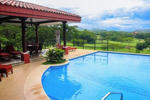 A swimming pool with a covered seating area and a view of a green landscape. - Playa Conchal Resort Condo w/ Ocean View (Playa Conchal)