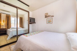 Ein Hotelzimmer mit zwei Betten, einem Fernseher, einem Spiegel und Kunstwerken an der Wand.