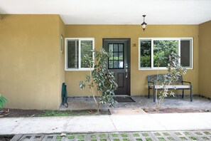 Ein Haus mit einer Haustür, zwei Fenstern, einer Bank und einem kleinen Baum.