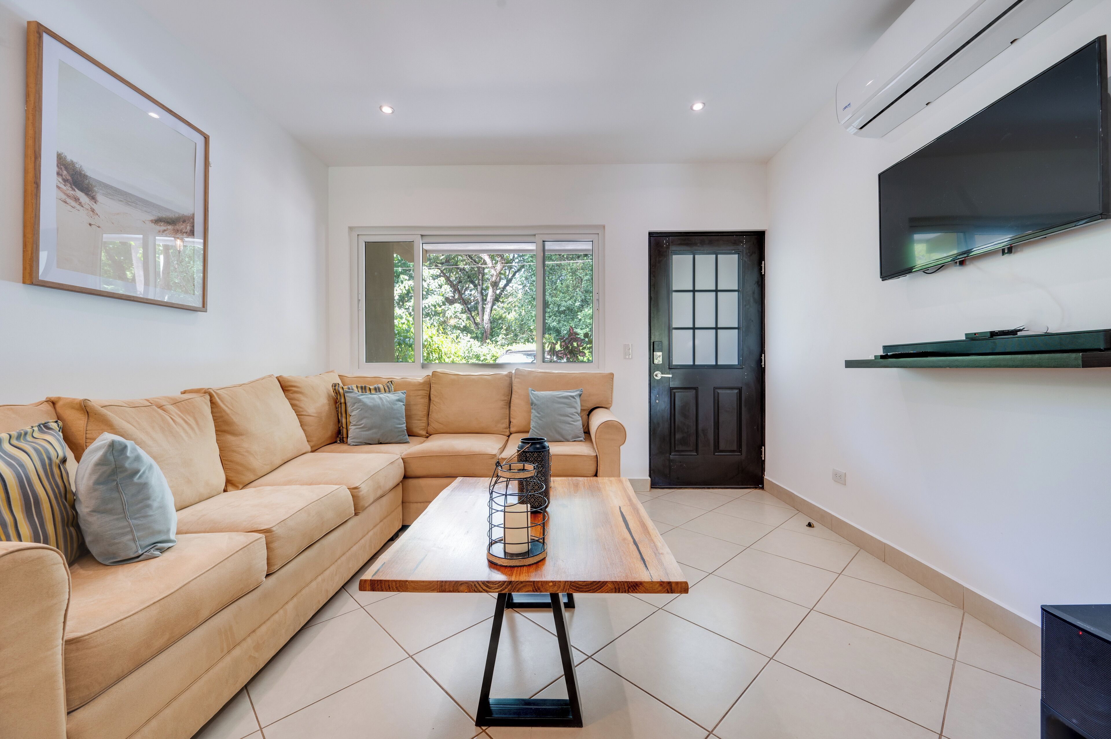 A living room with a beige sectional sofa, a wooden coffee table, a framed picture on the wall, and a door with a window.