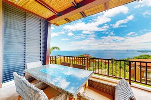 A balcony with a glass table and wicker chairs, overlooking a coastal view. - Playas del Coco Condo: Ocean Views, Shared Pool! (Playa Ocotal)