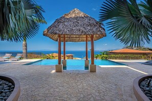 A thatched gazebo over a pool with a view of the sea. - Playas del Coco Condo: Ocean Views, Shared Pool! (Playa Ocotal)