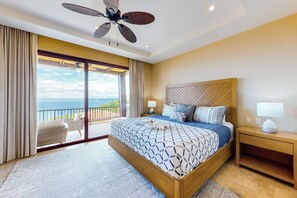 A bedroom with a large bed, a nightstand, a ceiling fan, and a view of the sea through a sliding door. - Playas del Coco Condo: Ocean Views, Shared Pool! (Playa Ocotal)