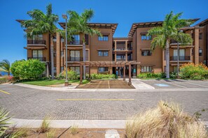 A multi-story hotel with a covered entrance, paved parking, and lush landscaping. - Playas del Coco Condo: Ocean Views, Shared Pool! (Playa Ocotal)