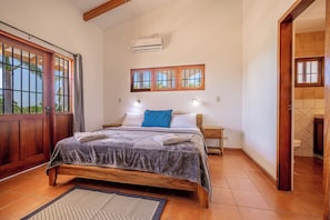 A bedroom with a bed, a nightstand, a window, and an air conditioning unit. - Santa Cruz Group Getaway w/ Pool: Walk to Beach (Junquillal)