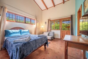 A bedroom with a bed, a chair, a table, and large windows. - Santa Cruz Group Getaway w/ Pool: Walk to Beach (Junquillal)